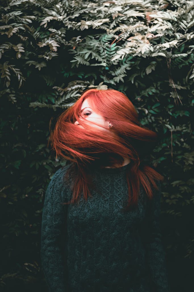 Stylish young woman shaking long foxy hair in lush green garden